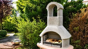 A stone-built outdoor grill with a chimney, surrounded by greenery.