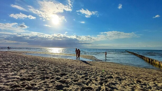 A beach with a pier extending into the water, people walking along the shore, and a clear sky.