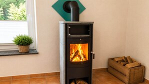 A wood-burning stove with a fire, a window with a plant, and a wood storage box.