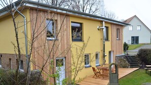 A modern house with a yellow facade, a wooden deck, and a stone fireplace.
