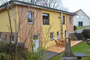 A modern house with a yellow facade, a wooden deck, and a stone fireplace. - Charmante Ferienwohnung Vincent in Strandnaehe (Poel)