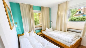 A room with two wooden beds, a small table, and a window with curtains.