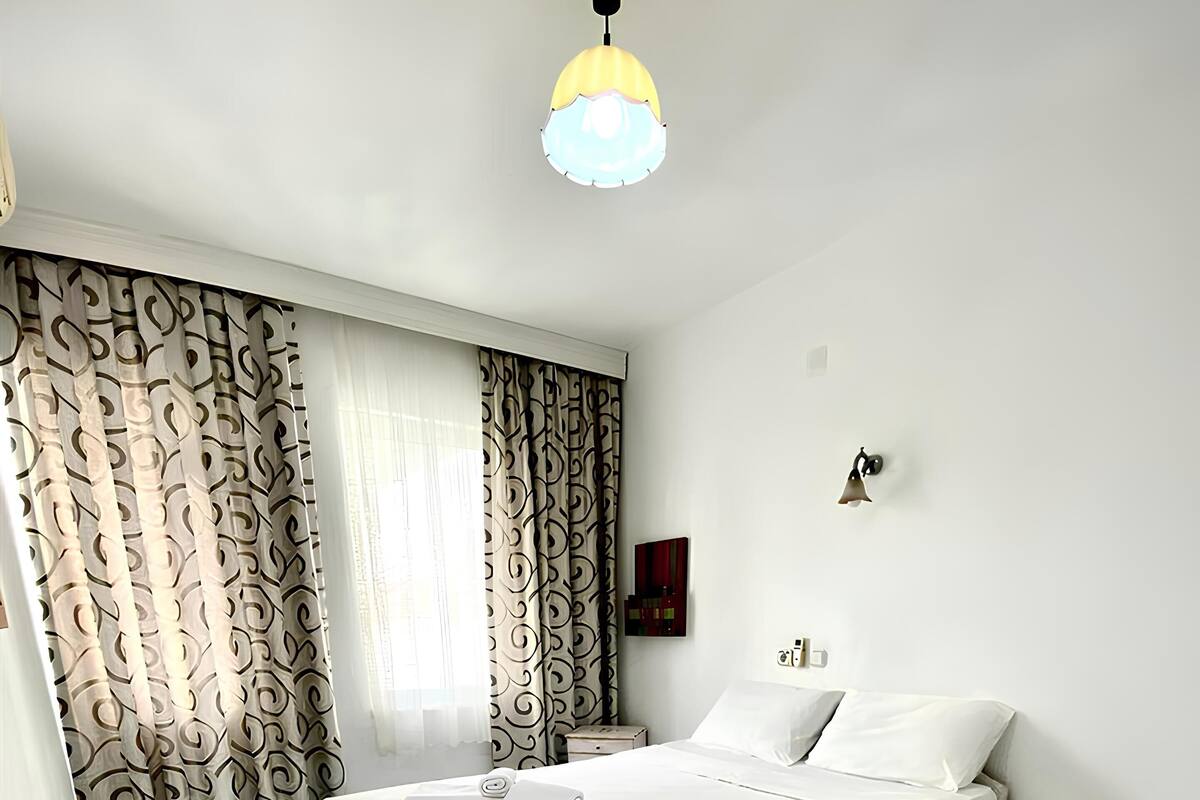 A hotel room with a bed, a nightstand, a lamp, and a window with curtains.