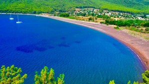 A coastal landscape with a beach, clear blue water, and sailboats. - Akdeniz Pansiyon (Koycegiz)
