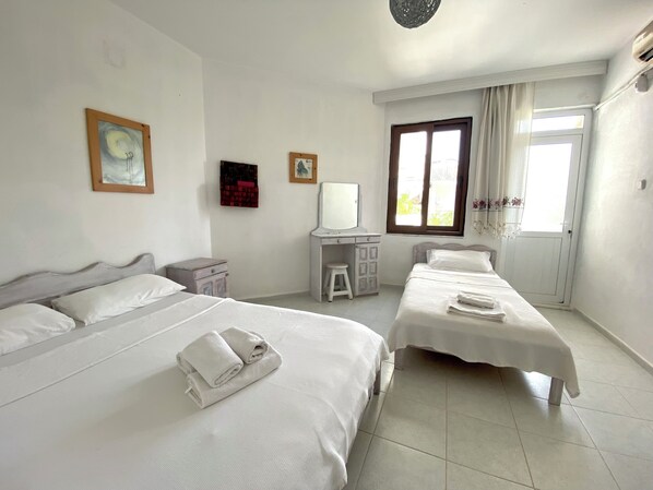 A hotel room with two beds, a desk, a chair, and a window with curtains. - Akdeniz Pansiyon (Koycegiz)