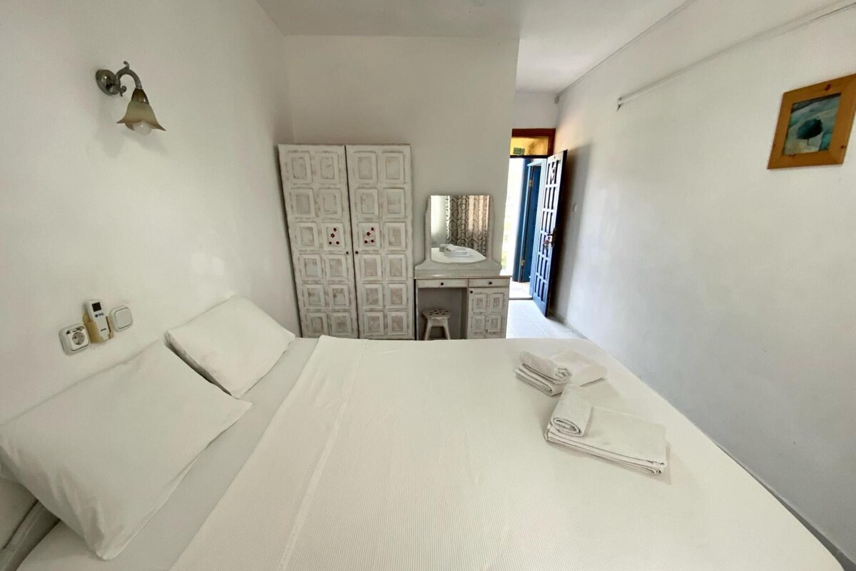 A hotel room with a bed, a desk, a wardrobe, and a bathroom visible through an open door.