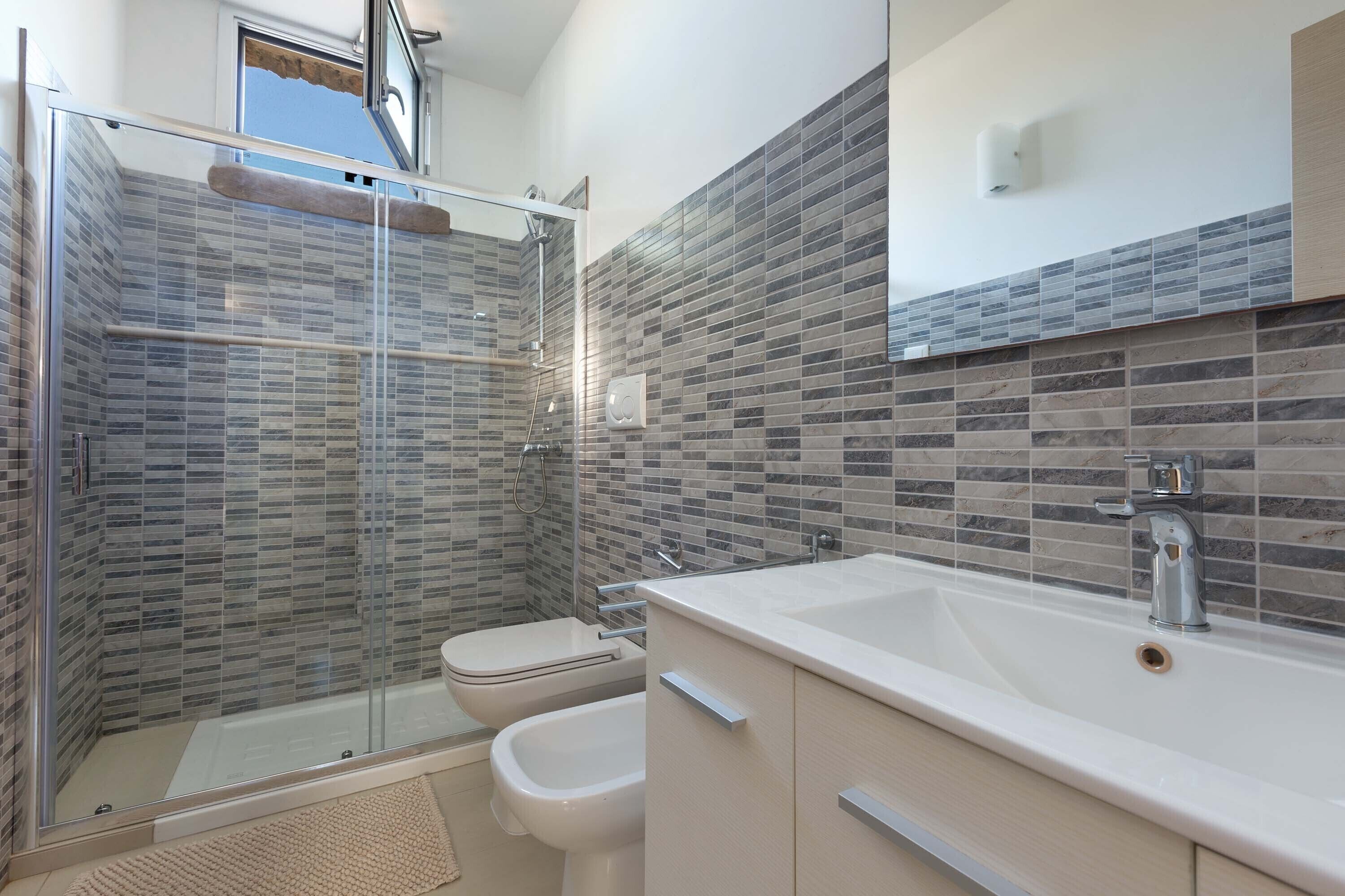 Een moderne badkamer met een douchecabine van glas, een badkuip, een toilet en een wastafelmeubel met een wastafel.