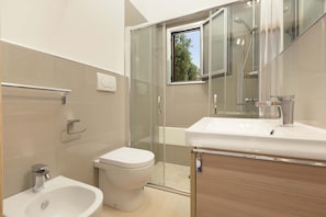 A modern bathroom with a bidet, toilet, glass shower enclosure, and a sink.