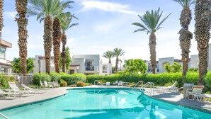 A swimming pool surrounded by palm trees and lounge chairs, with a clear blue sky above.