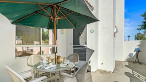 A patio with a table set for four, surrounded by white chairs, under a green umbrella.