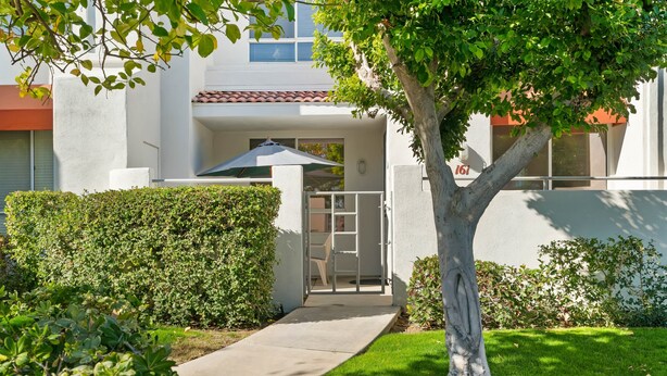 A modern building with a covered entrance, a concrete pathway, and a well-maintained lawn.