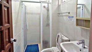 A bathroom with a shower, toilet, sink, and a blue mat on the floor. - RM Grandview Residences (Baguio)