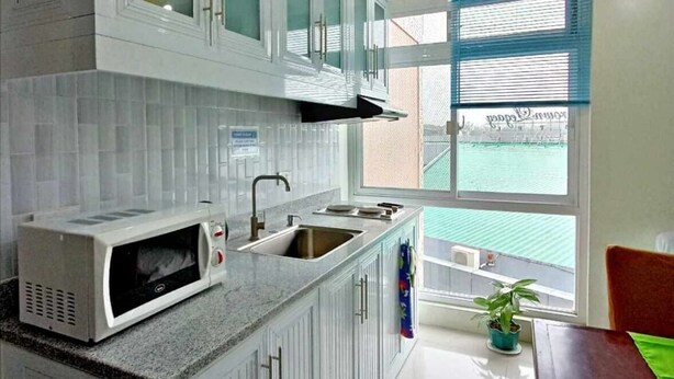 A modern kitchen with white cabinets, a built-in microwave, a sink, and a window with a view of a green landscape. - RM Grandview Residences (Baguio)