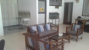 A living room with a sofa set, two armchairs, a coffee table, and a side table. There is a window with curtains, a wall-mounted shelf, and a framed picture. - Larn's villa. (Wadduwa)