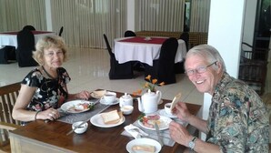 A dining area with tables set for two, featuring white tablecloths, black chairs, and a variety of breakfast items including toast, eggs, and coffee. - Larn's villa. (Wadduwa)