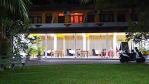 A hotel with a covered outdoor seating area, a parked scooter, and a well-maintained lawn. - Larn's villa. (Wadduwa)