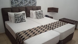 A double bed with a patterned bedspread and pillows, a bedside table with a phone, and a wall-mounted shelf. - Larn's villa. (Wadduwa)