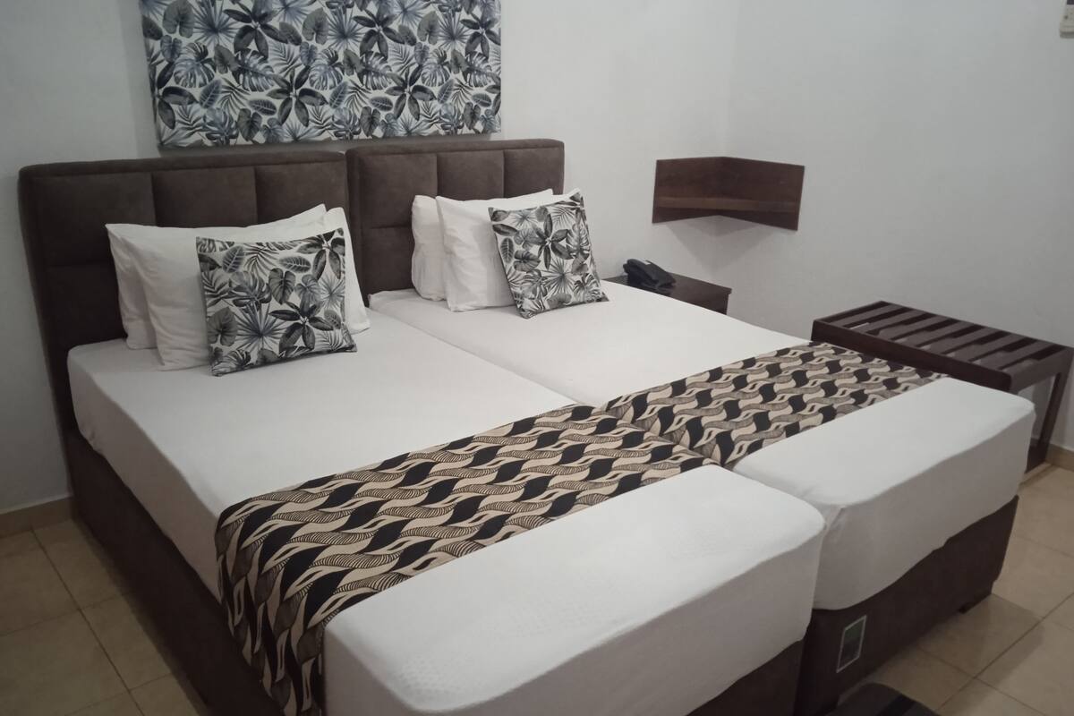 A double bed with a patterned bedspread and pillows, a bedside table with a phone, and a wall-mounted shelf.