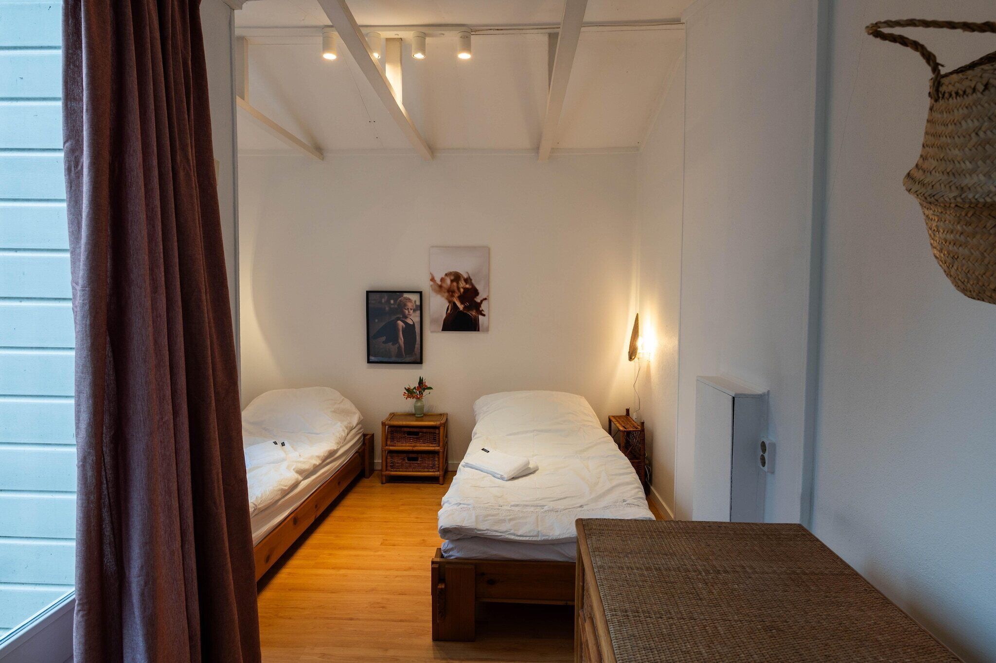 Une petite chambre accueillante avec deux lits simples, un plancher en bois, une petite table et un panier fixé au mur.