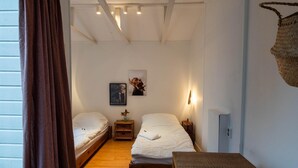 Ein kleiner, gemütlicher Raum mit zwei Einzelbetten, Holzboden, einem kleinen Tisch und einem Wandkorb.