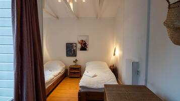 Une petite chambre accueillante avec deux lits simples, un plancher en bois, une petite table et un panier fixé au mur.