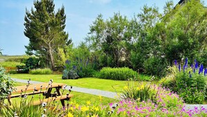 Un giardino con una panchina di legno, un vialetto e diverse piante fiorite.