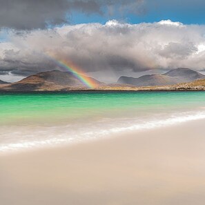 A beach with clear turquoise water, a rainbow, and mountains in the background. - Pabbay House (Isle of Lewis)