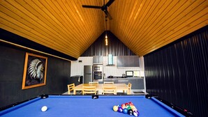A pool table with balls, a ceiling fan, a dining table with chairs, and a kitchen area in the background. - NP Pool Villa Hua Hin (Hua Hin)