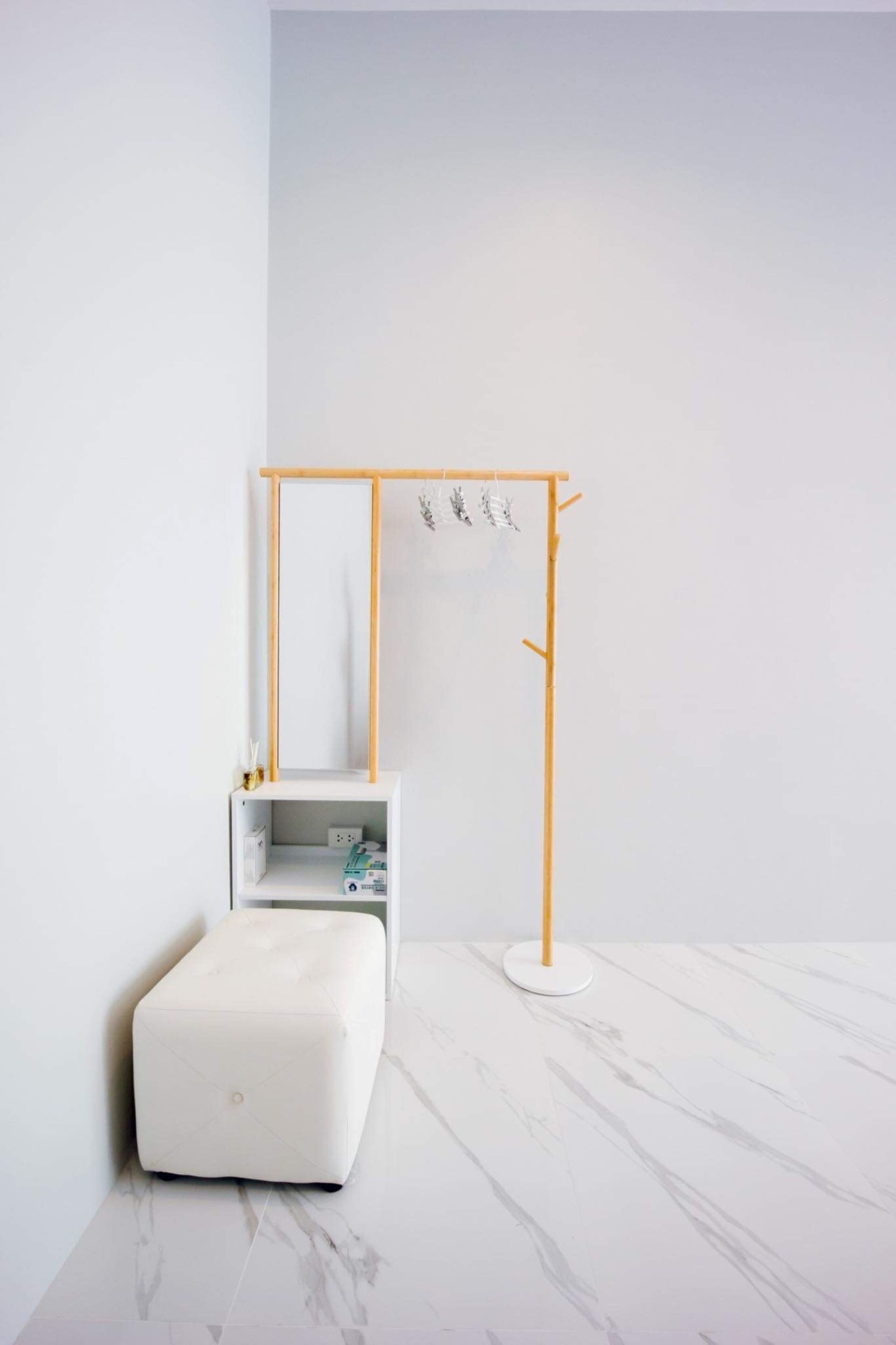 Habitación minimalista con un armario blanco, un pequeño reposapiés blanco y un perchero de madera.