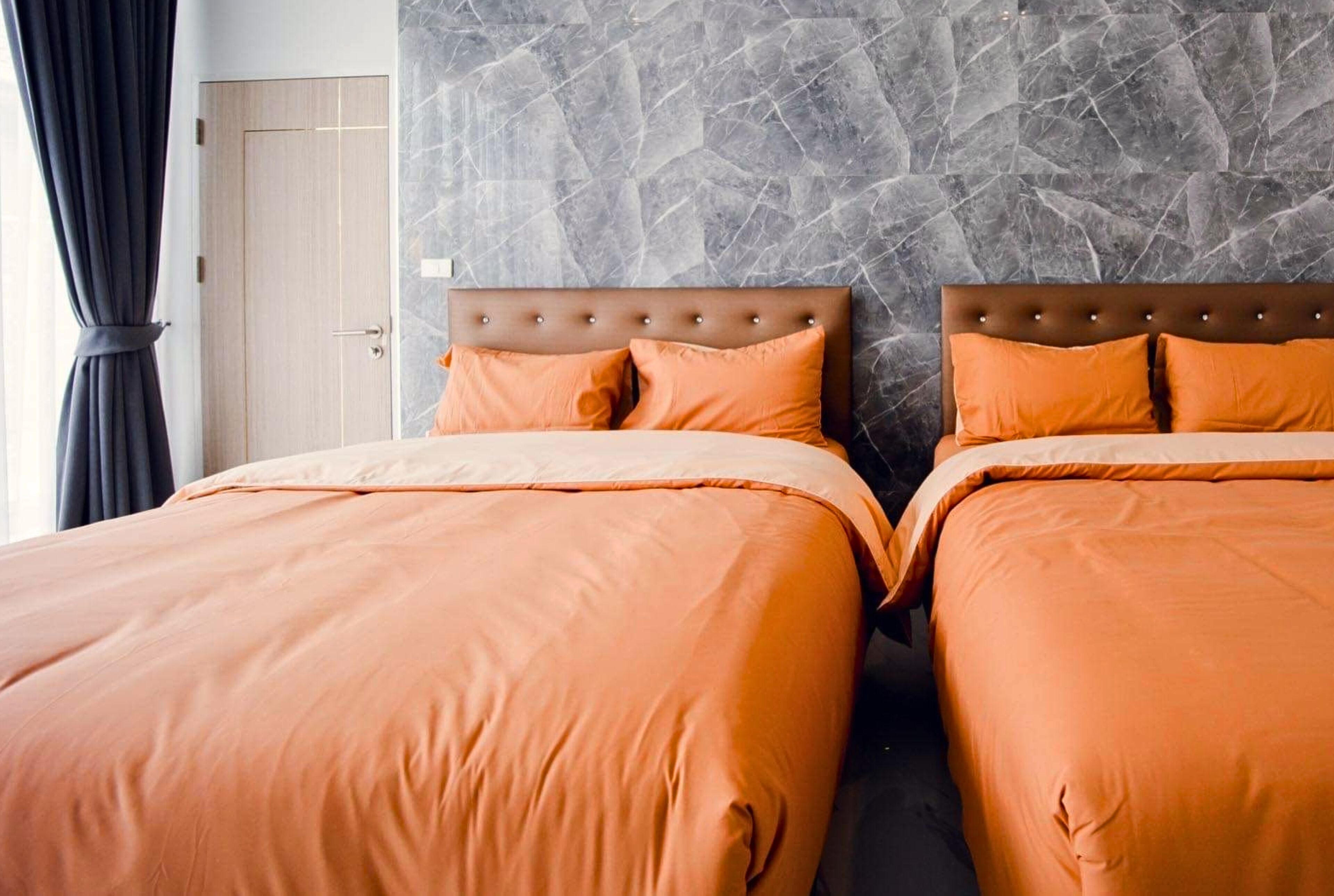 Une chambre d’hôtel avec deux lits, un mur décoré d’un motif imitant le marbre et une porte en bois.
