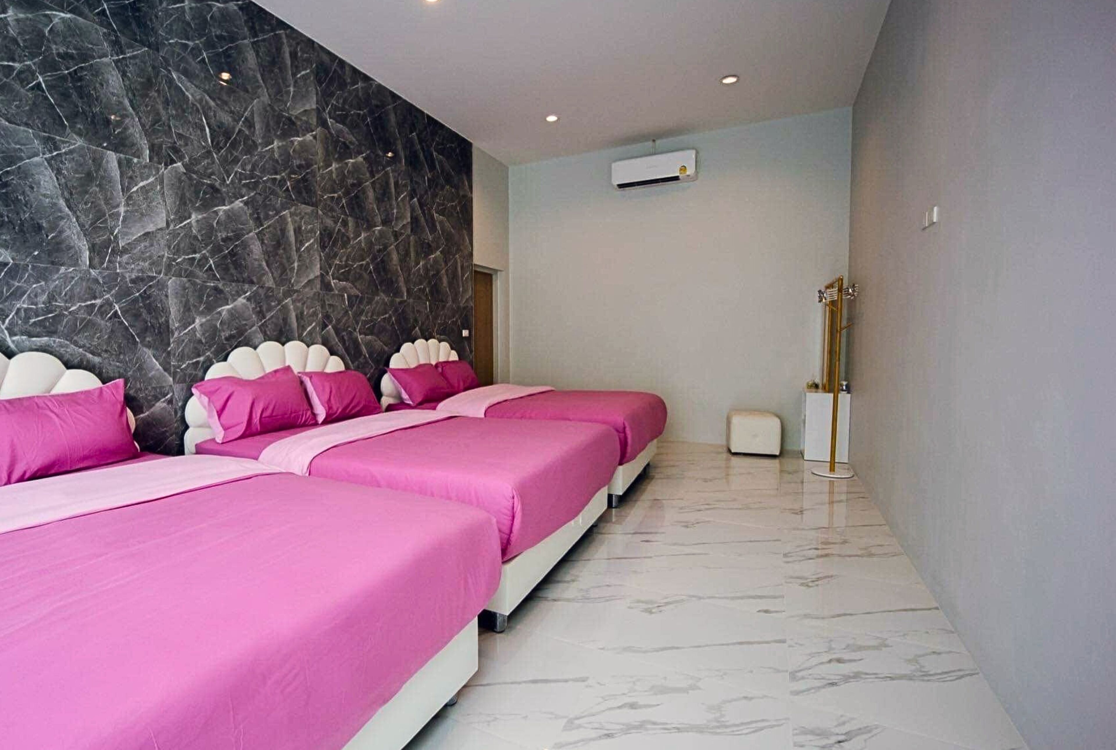 A modern hotel room with a marble wall, a large bed with pink bedding, and a small bedside table.