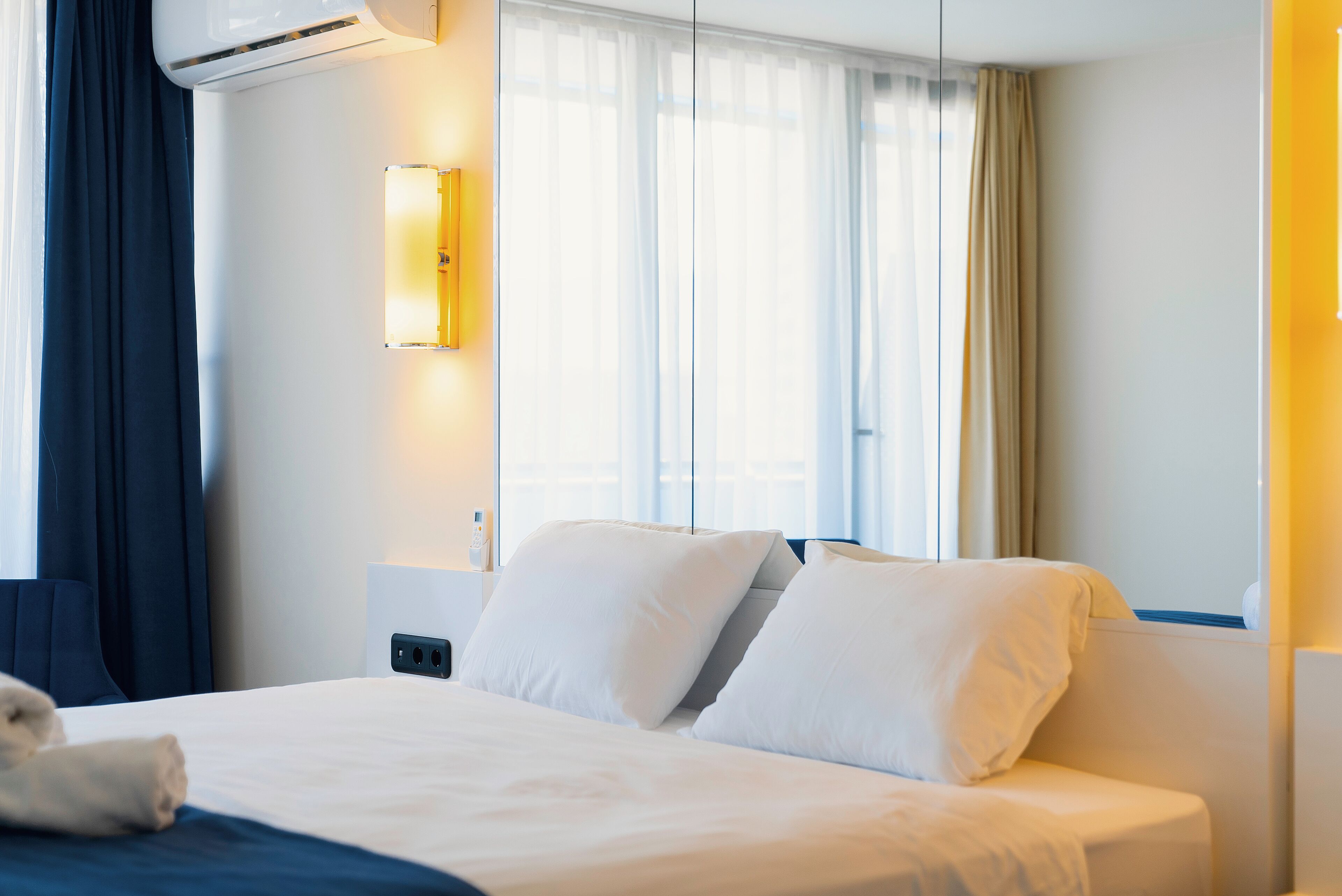 A hotel room with a bed, a bedside table, a lamp, and a window with curtains.