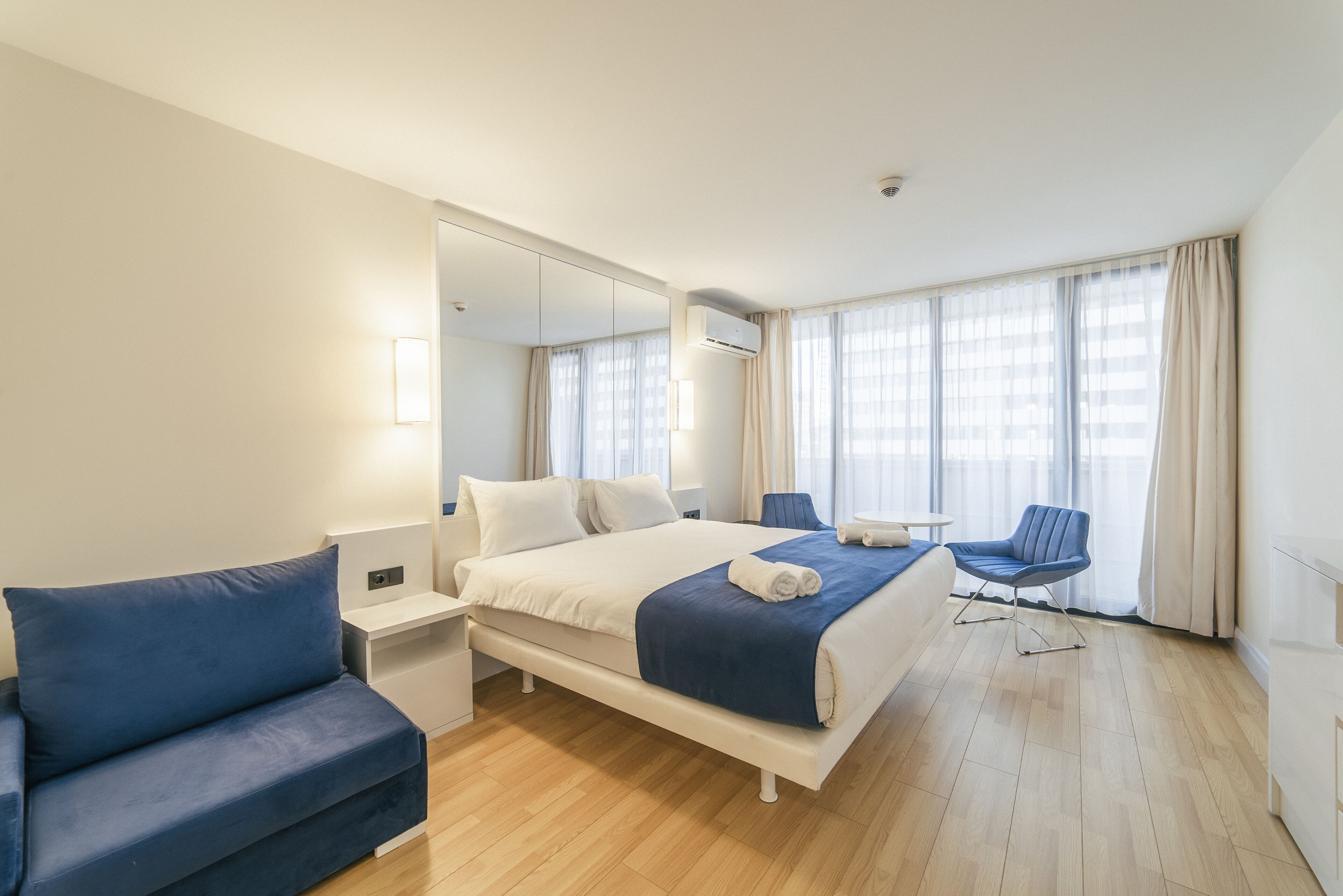 A hotel room with a bed, a blue sofa, a small table, and a chair.