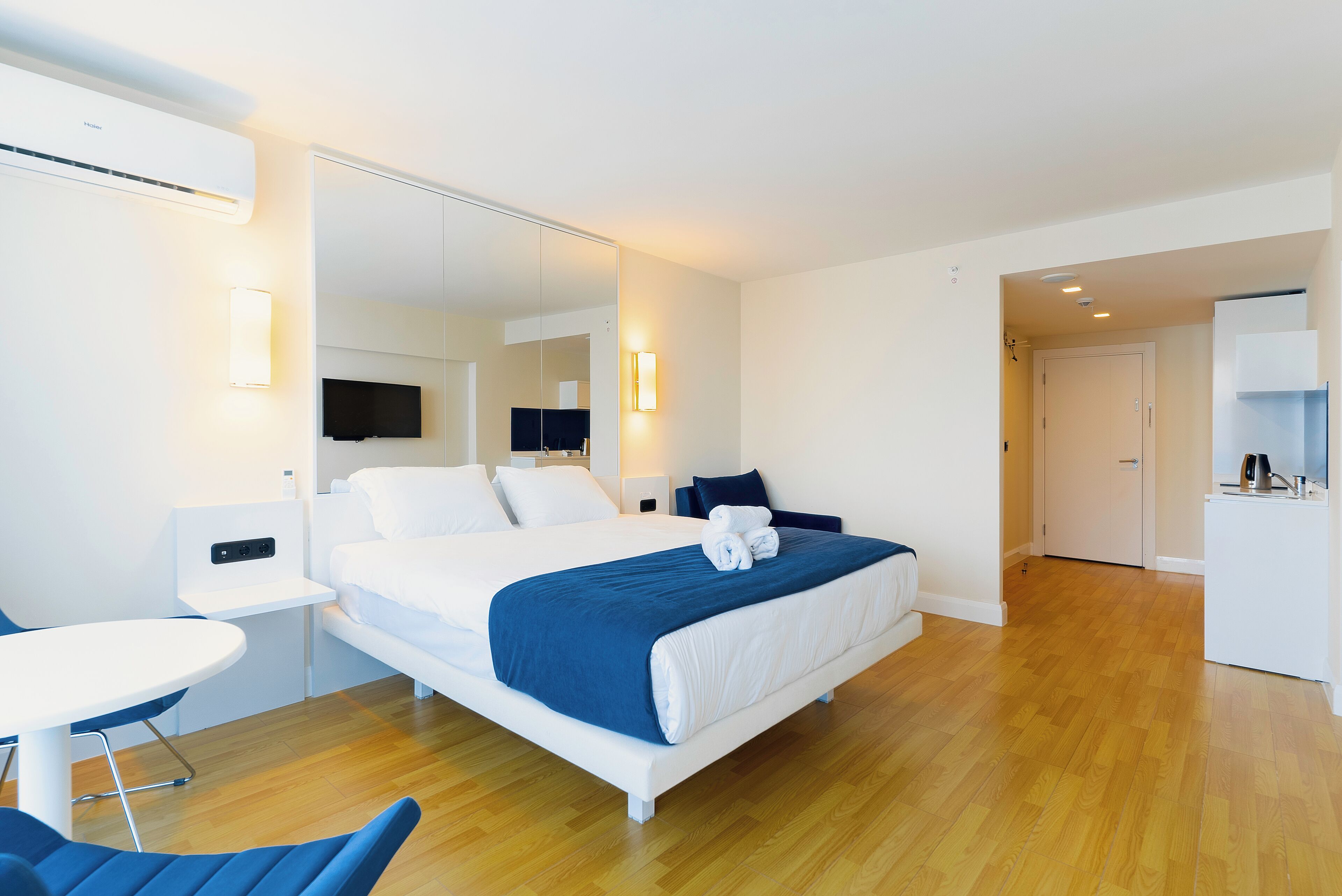 Une chambre d’hôtel moderne équipée d’un grand lit, d’un petit bureau, d’une chaise, d’une télévision et d’un coin cuisine.