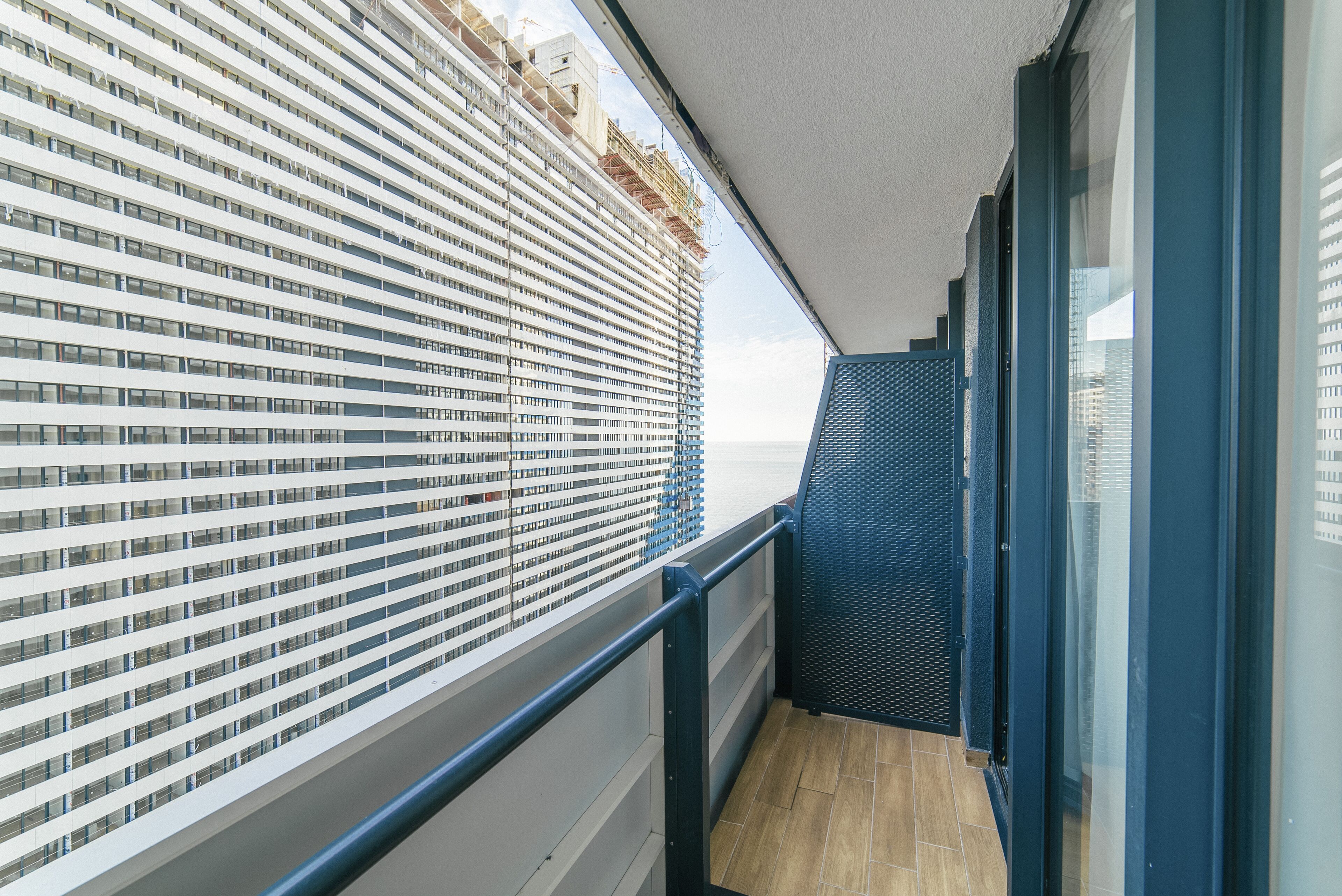 Een balkon met uitzicht op een modern gebouw, een glazen deur en een houten vloer.