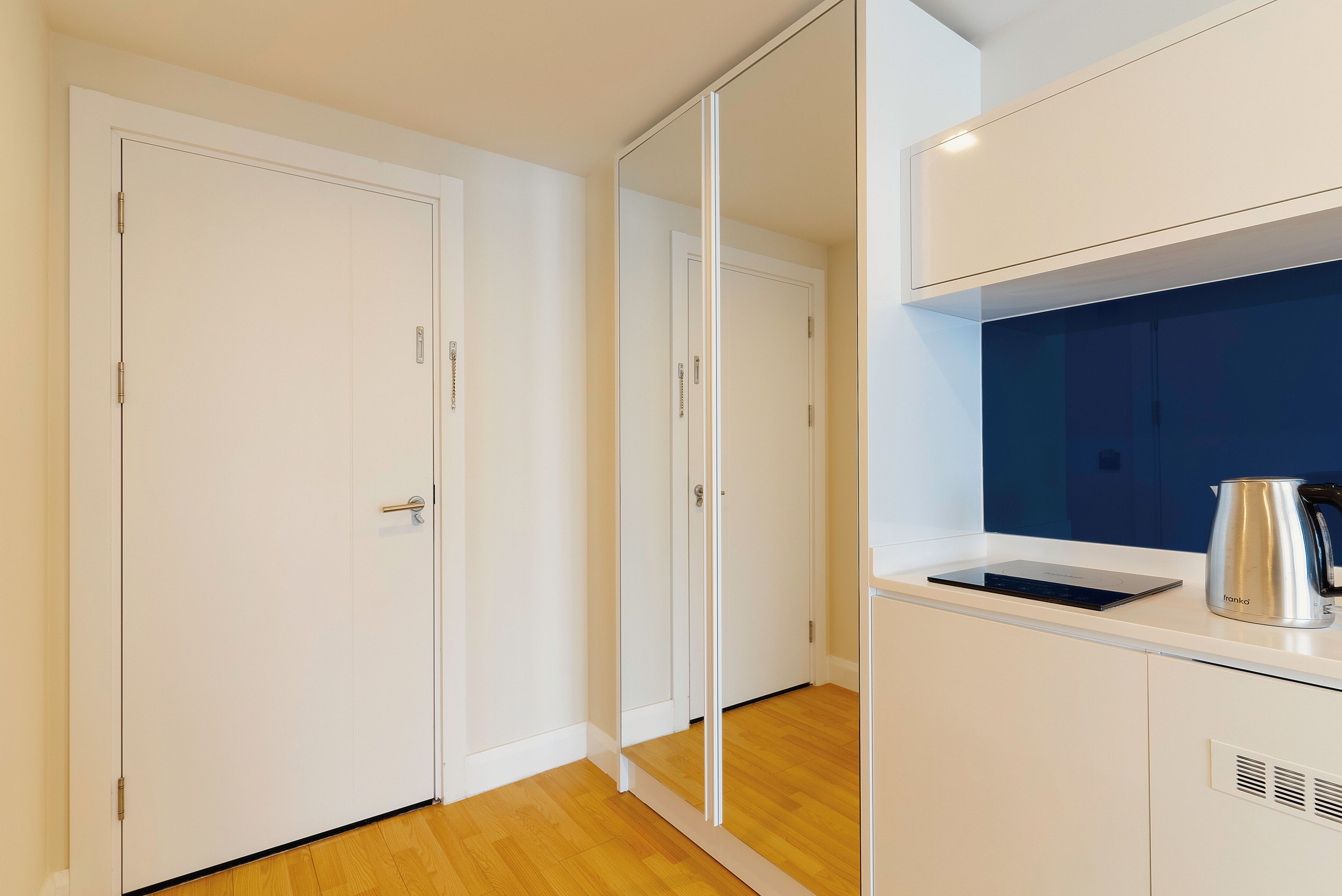 A modern kitchen with white cabinets, a stainless steel kettle, and a built-in oven.