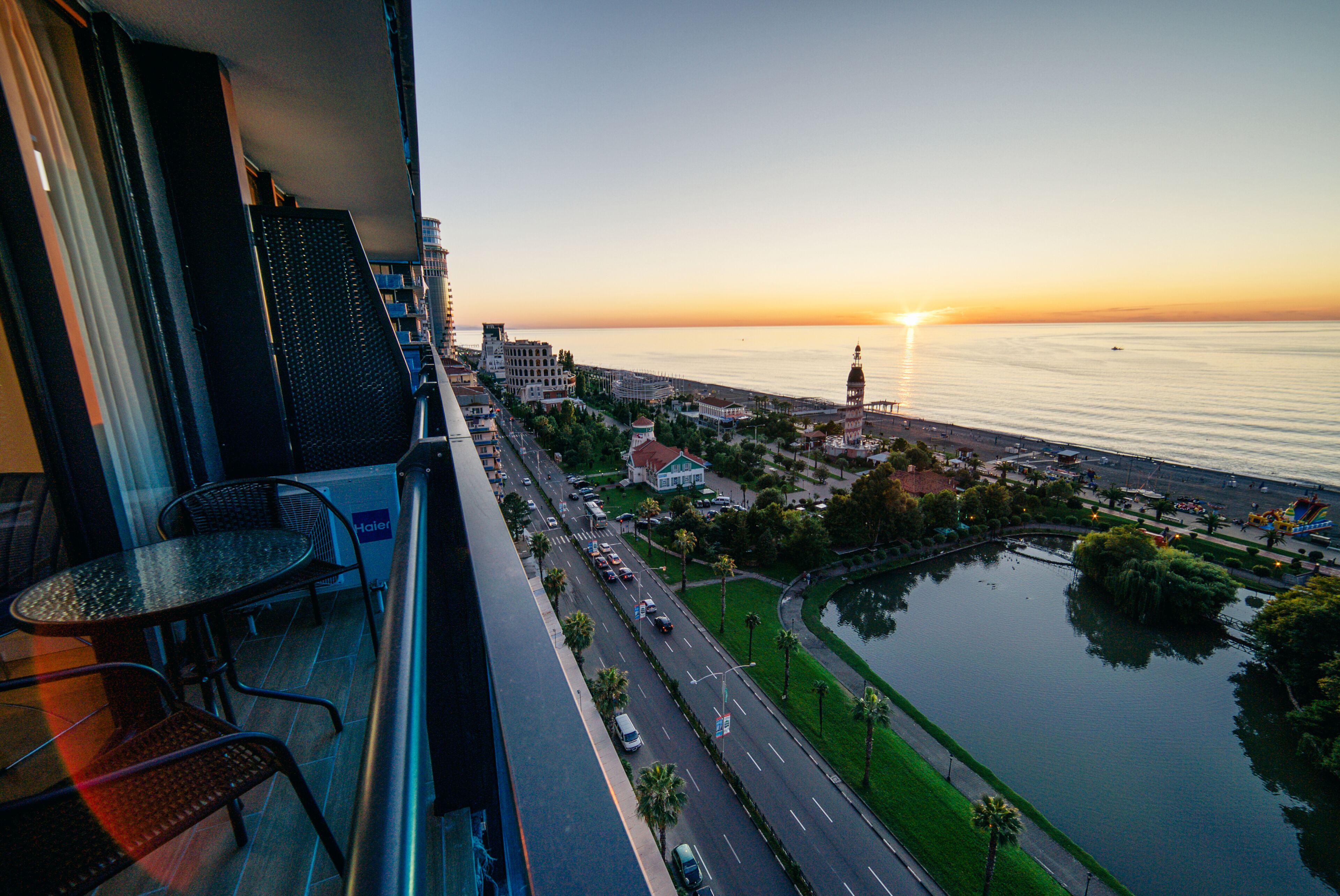 Un balcone con vista su una città al tramonto, una strada e uno specchio d'acqua.