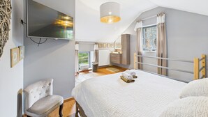 Un dormitorio con cama, una silla, un televisor, una ventana con cortinas y una lámpara colgante.