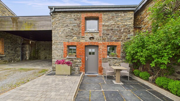 Un edificio de piedra con una puerta gris, una pequeña ventana y un patio empedrado con una mesa y sillas.
