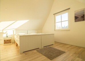 Un dormitorio con techo inclinado, una cama, una mesita de noche, un ventanal y vistas al exterior.
