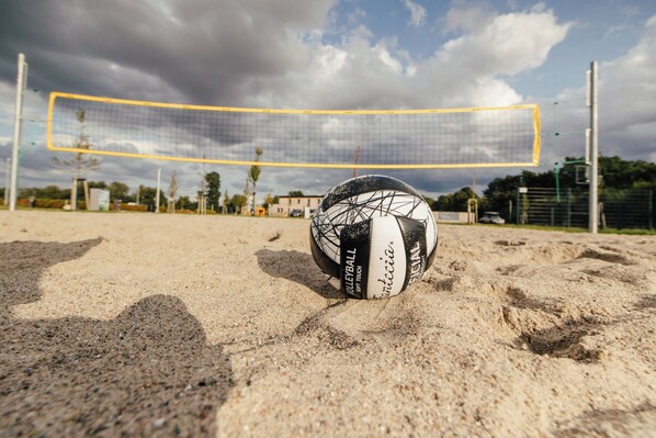 A volleyball on a sandy court with a net in the background.