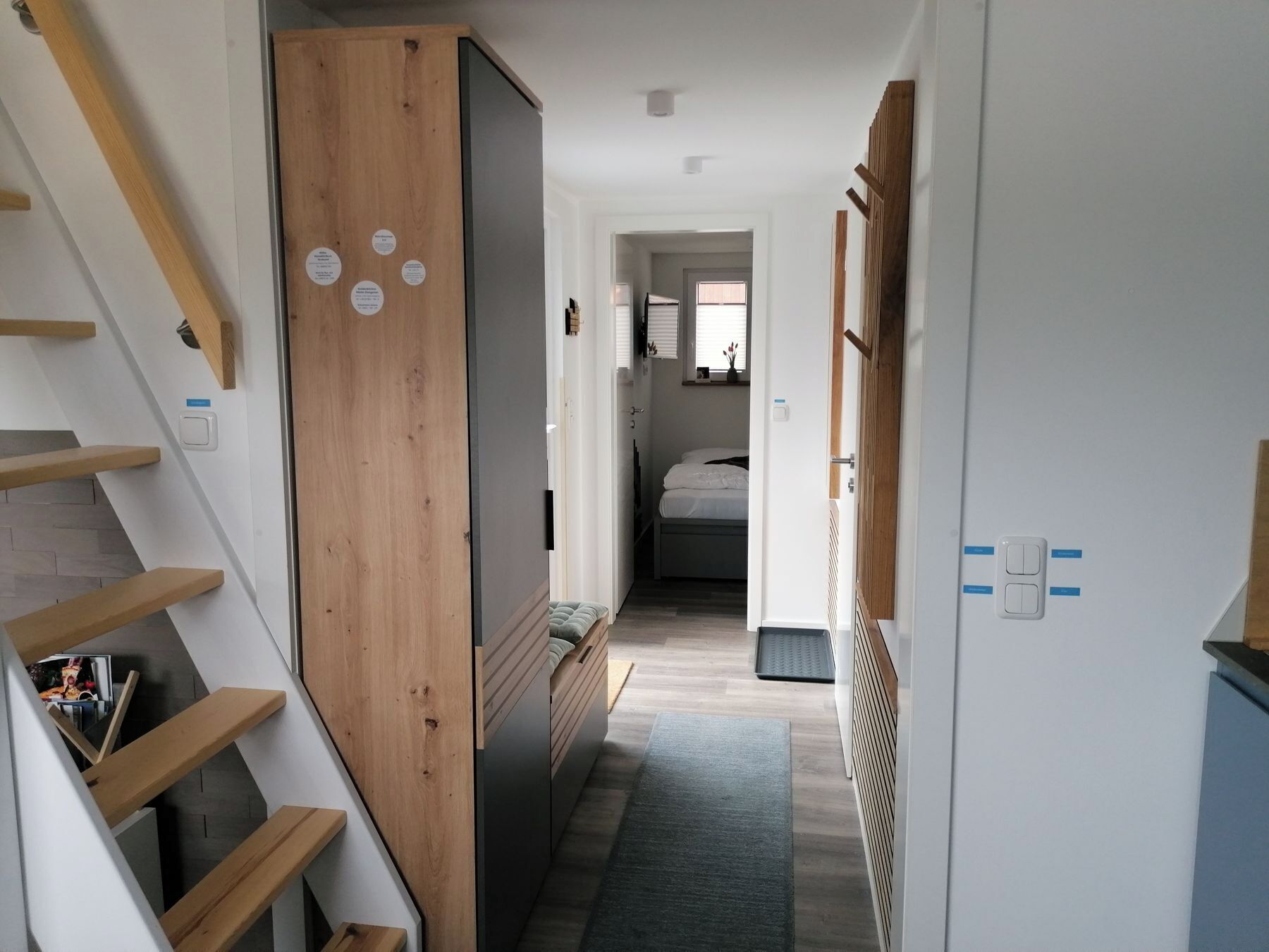 A narrow hallway with a wooden wardrobe, a bed, and a small sitting area.