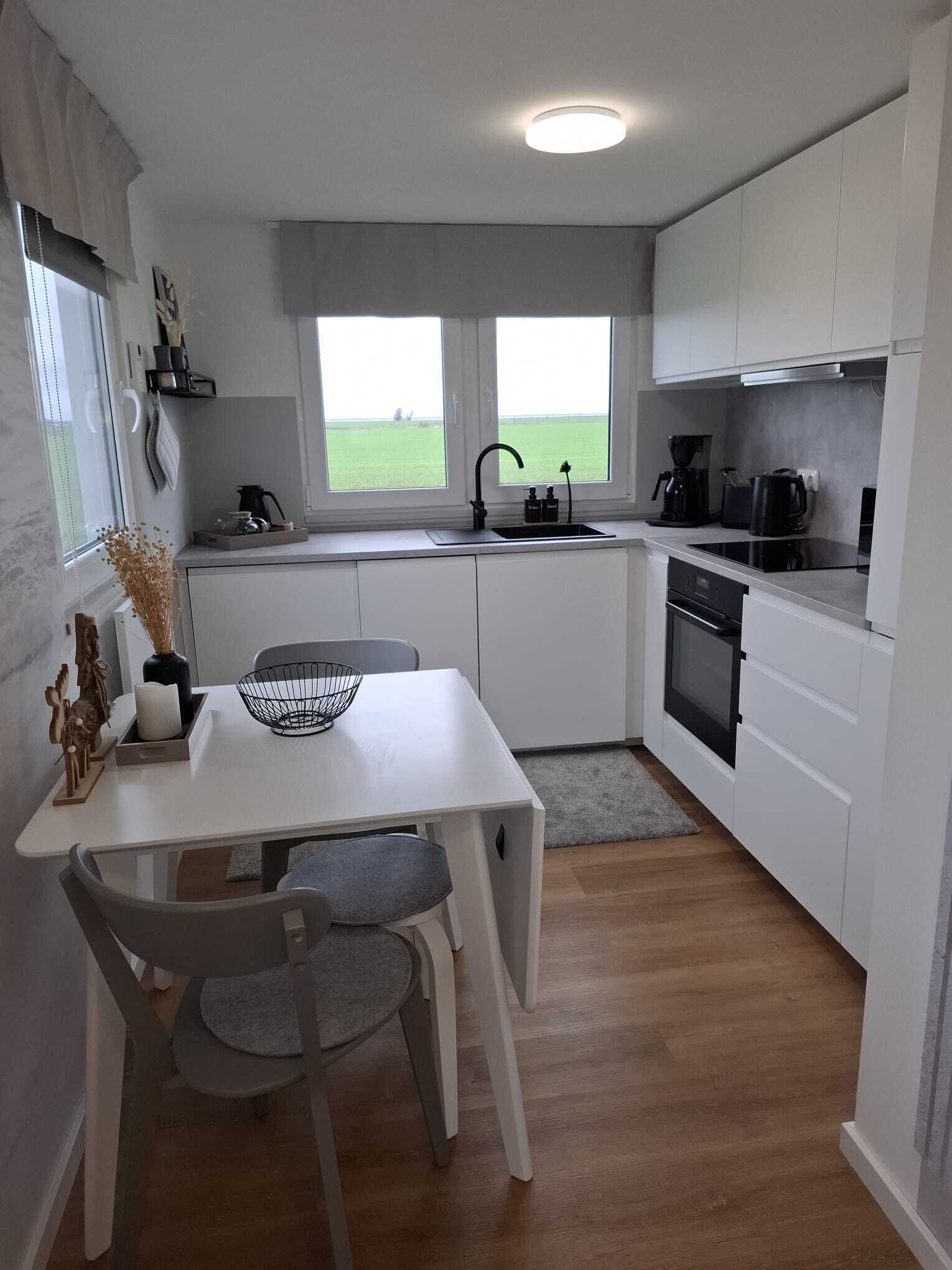 A modern kitchen with white cabinetry, a dining table with chairs, a window with a view of the outdoors, and a built-in oven.