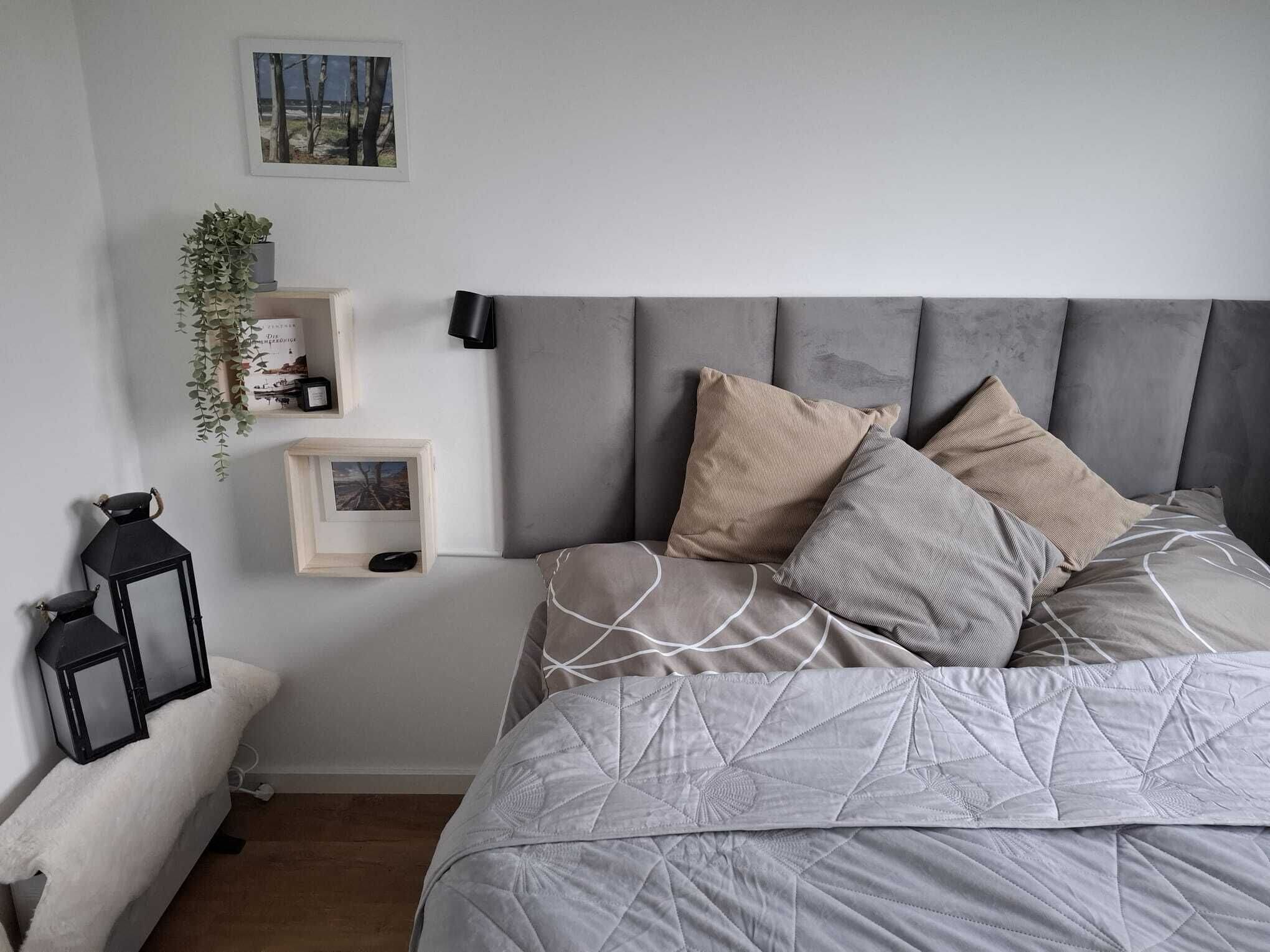 Un dormitorio con cama, mesitas de noche, un estante en la pared con plantas y un cuadro enmarcado.