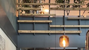 Interior de restaurante moderno con vigas de madera, lámparas colgantes y una variedad de opciones de asientos, incluyendo un banco largo y mesas individuales.