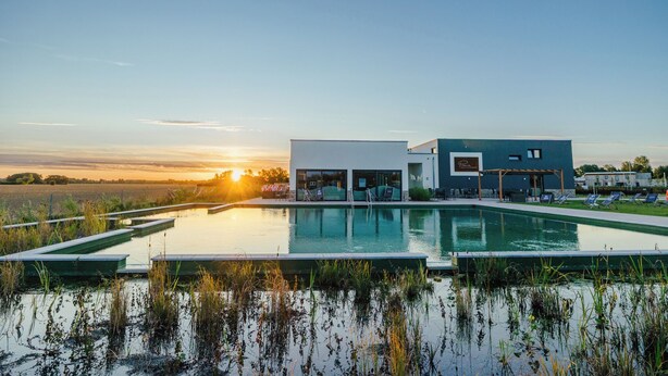 Un edificio moderno con piscina, mobiliario exterior y vistas al atardecer.