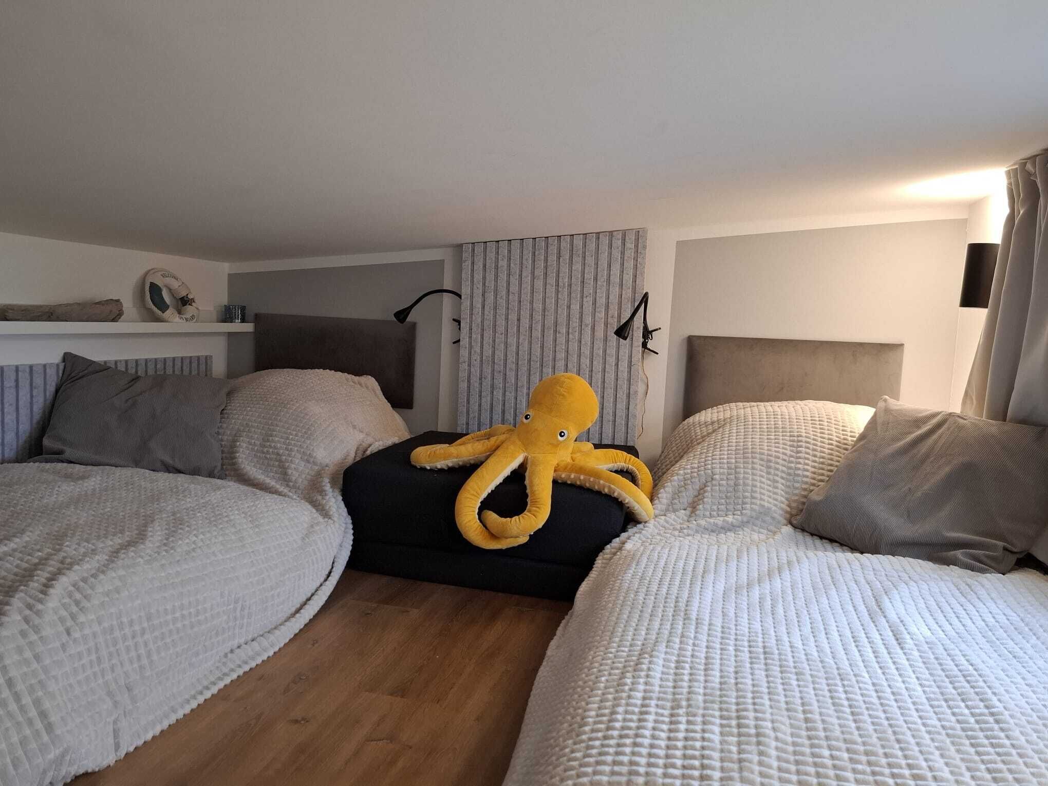 A hotel room with two beds, a large octopus plush toy on one bed, and a headboard with a light fixture.