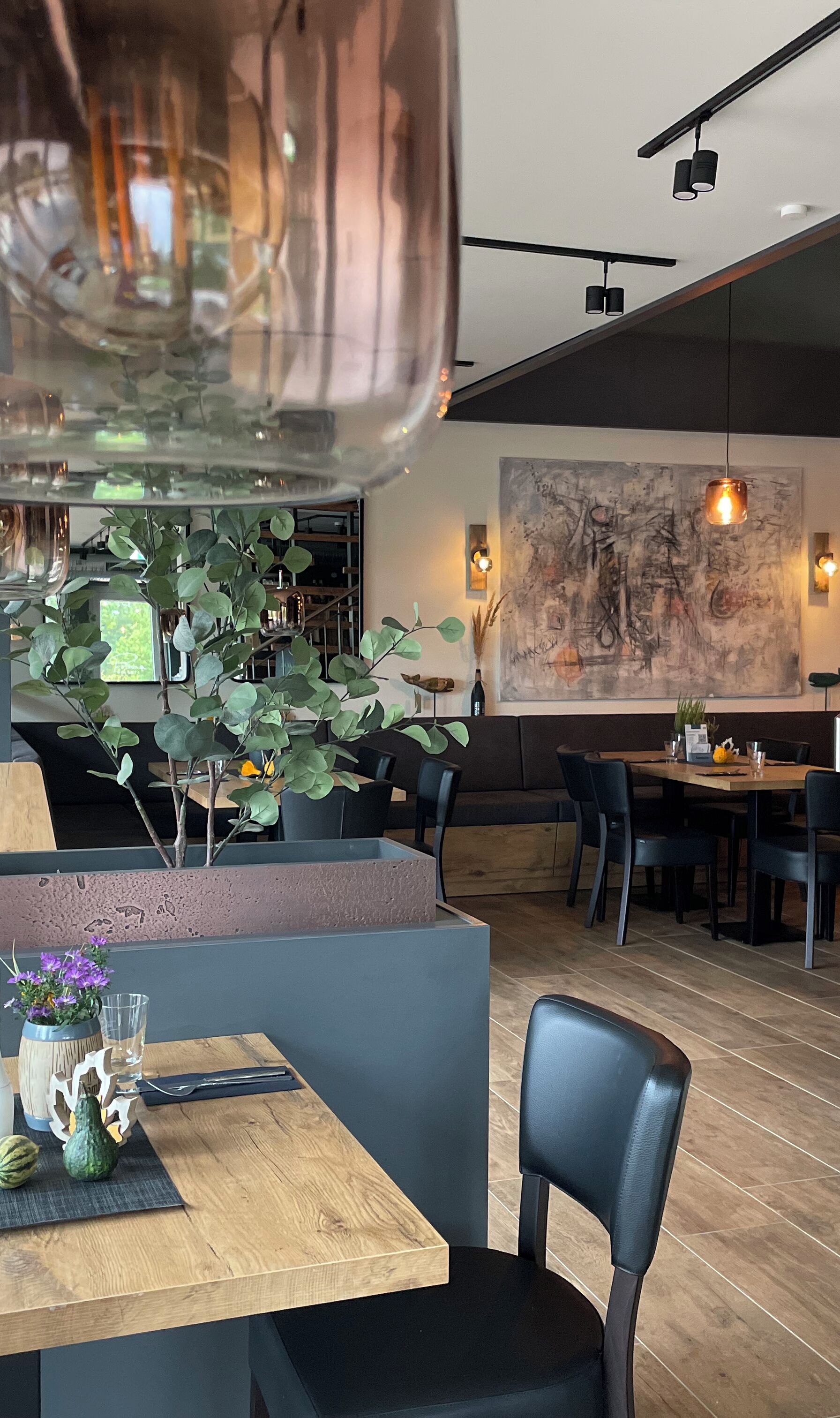 A modern restaurant interior with a wooden table, black chairs, and a large abstract painting on the wall.