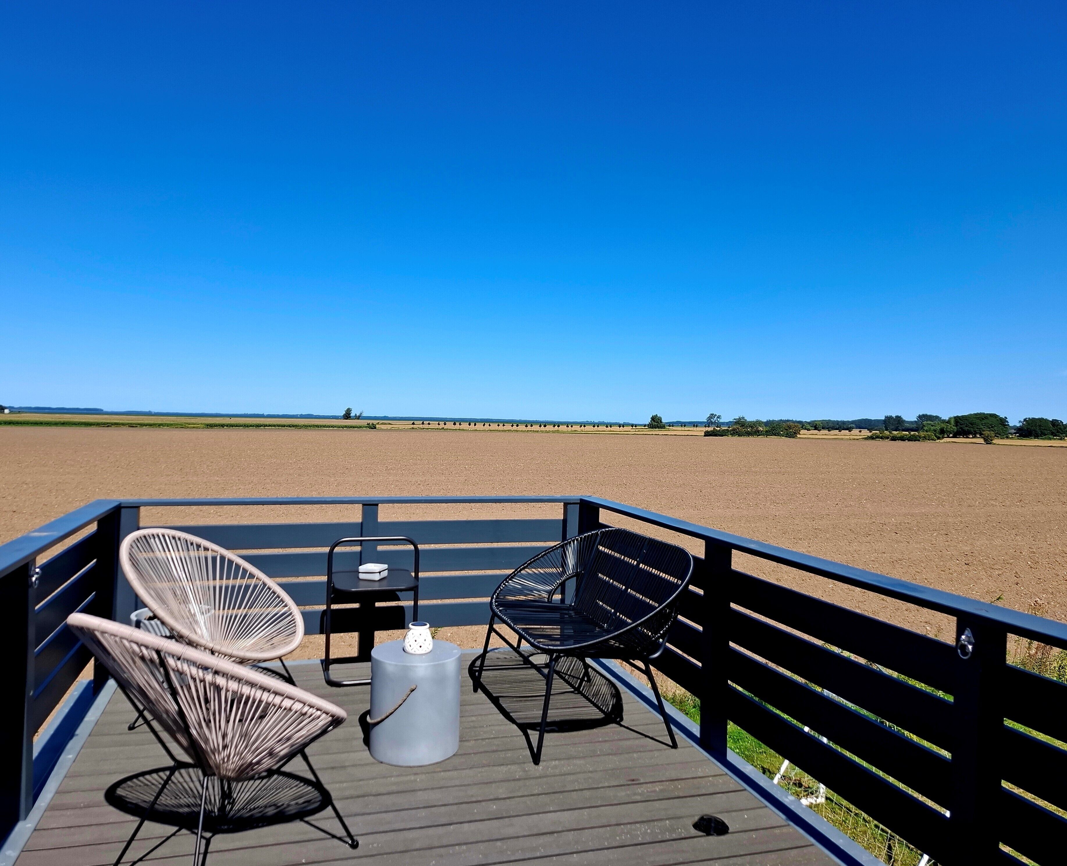 A deck with two wicker chairs and a small table, overlooking a vast open field.