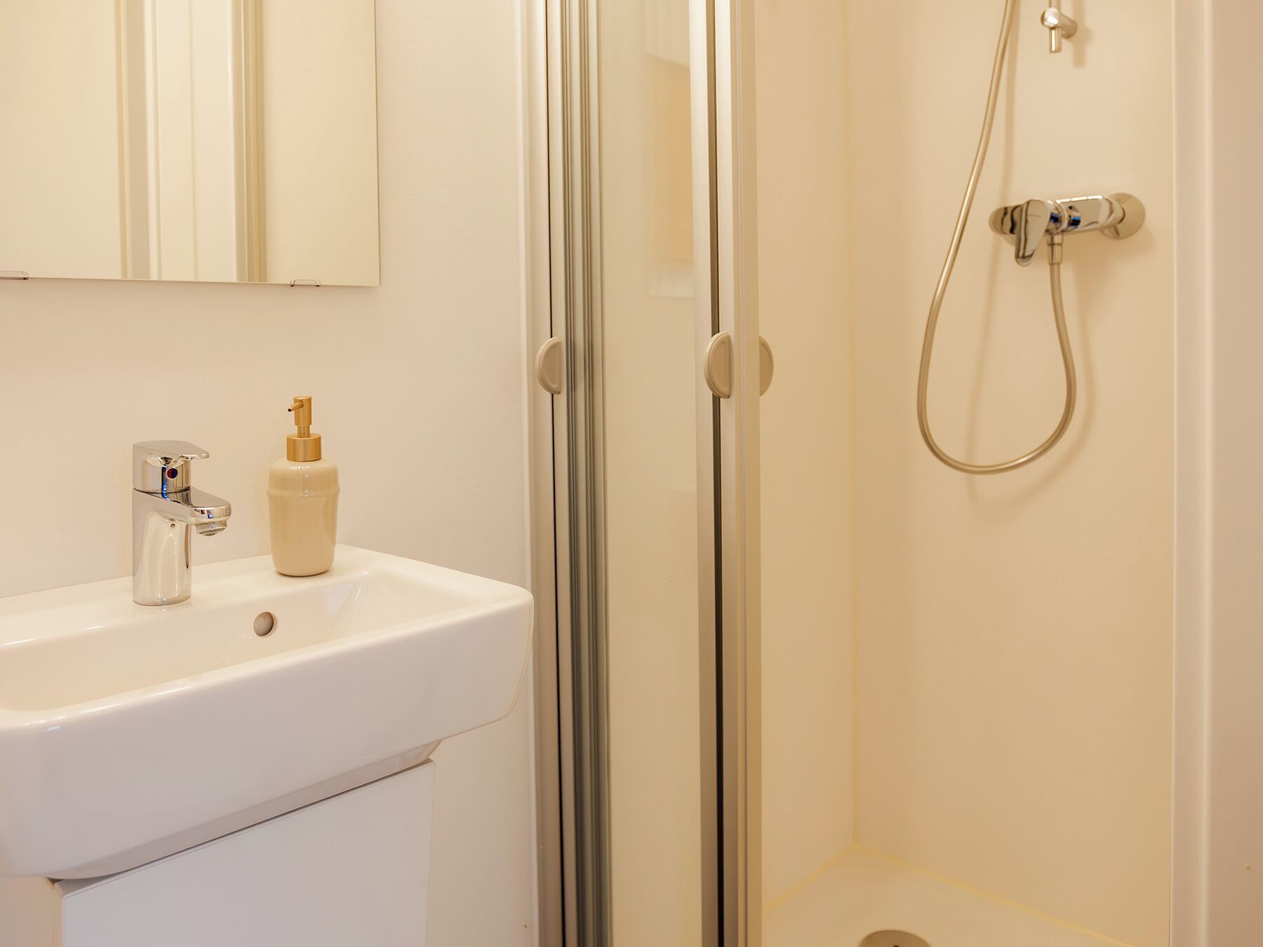 A bathroom with a white sink, a mirror, and a shower with a handheld showerhead.